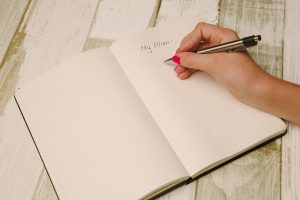 A notebook with the words 'My plan' in it lies open on a table. A right hand with red nail polish is poised over the notebook holding a pen.