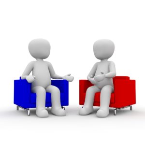 Two white cartoon figures, one sat on a blue chair, one on a red chair, having a conversation