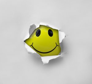 A yellow smiley face emoji is bursting through a white sheet of paper