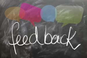 A blackboard on which the word feedback is written in white chalk. There are 4 differnt coloured speech bubble shapes above the word.
